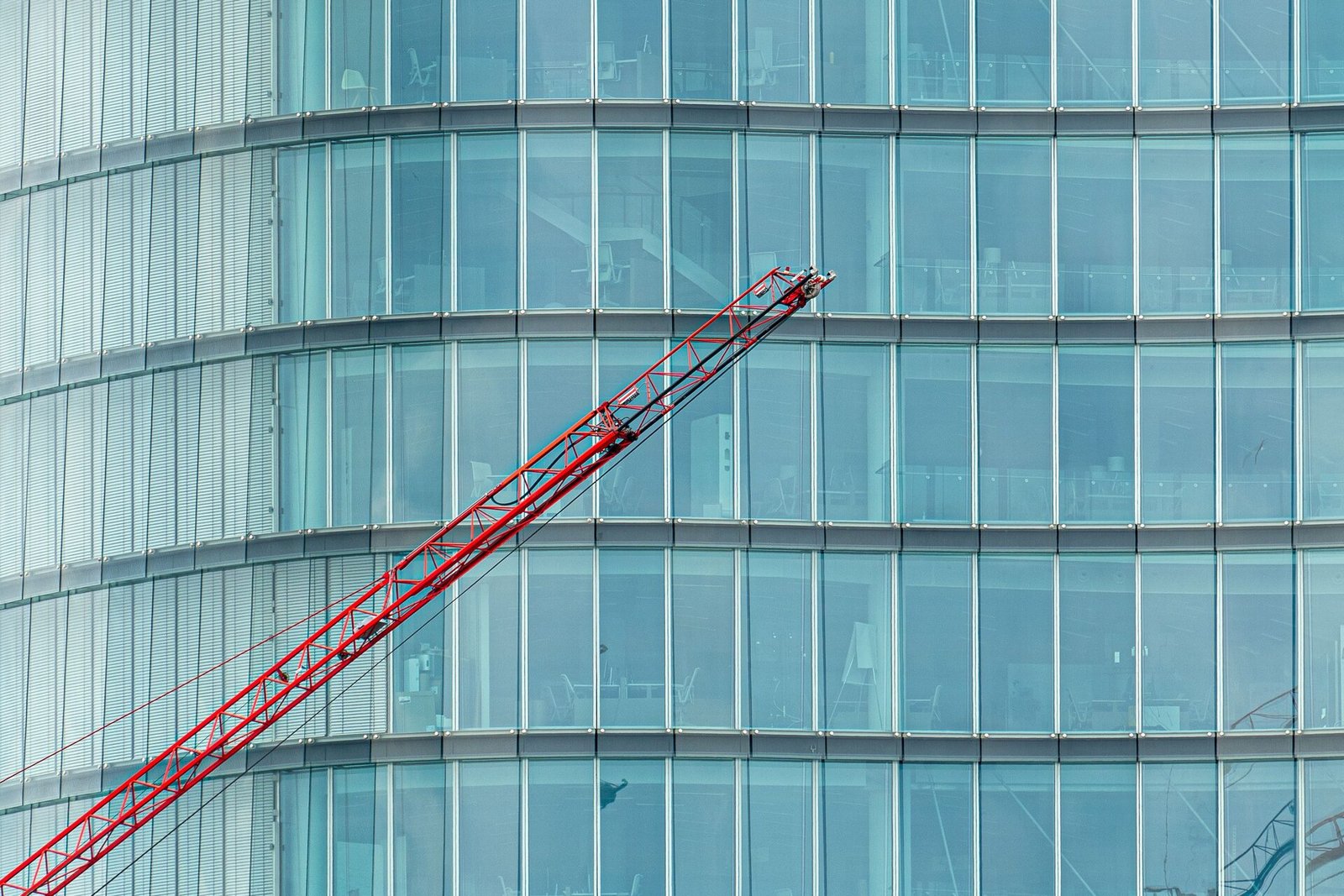 Red tower crane against a glass office tower facade